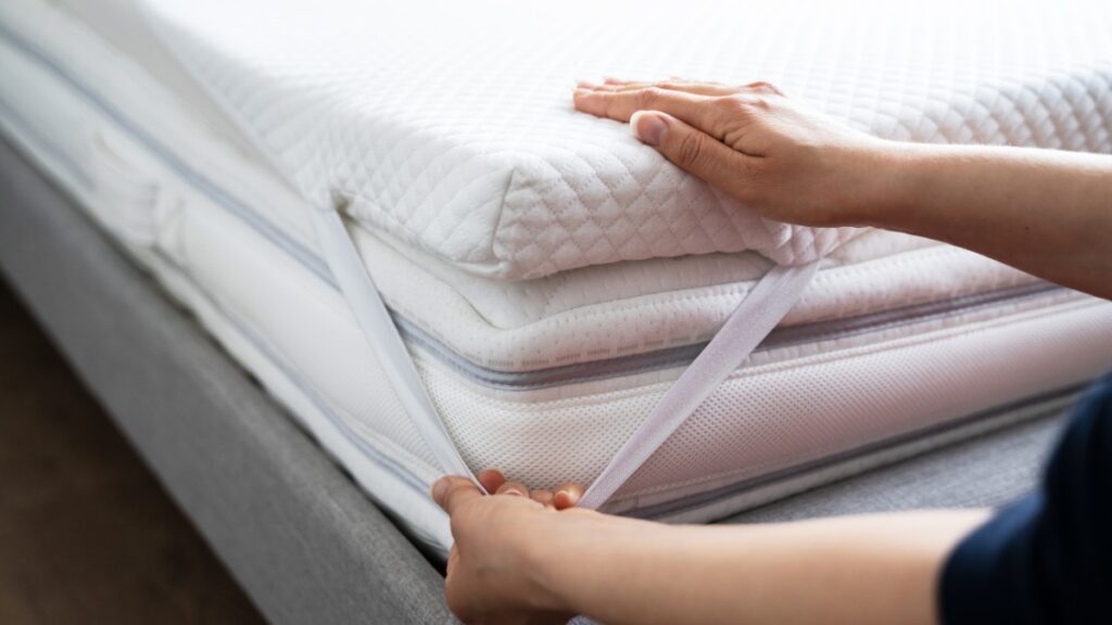 two hands putting a mattress topper on a mattress